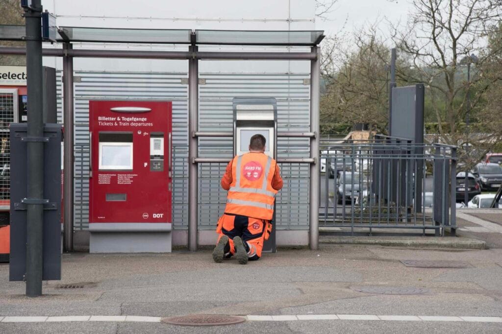 Servicetechniker von Wicotec Kirkebjerg in Warnweste kniet vor einem Fahrkartenautomaten der dänischen Staatsbahn DSB